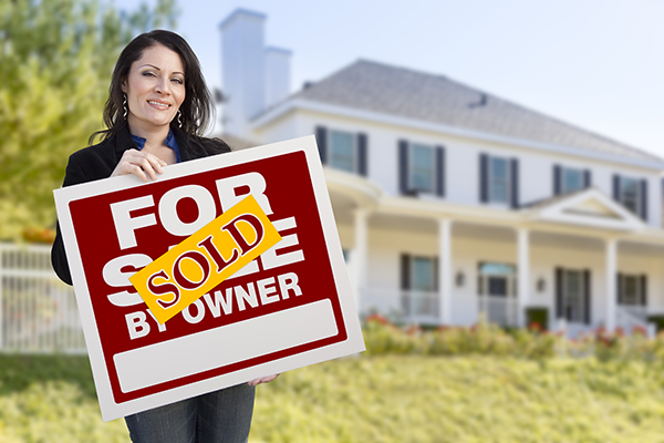 Smiling Hispanic Female Holding Sold For Sale By Owner Sign In Front of Beautiful House.